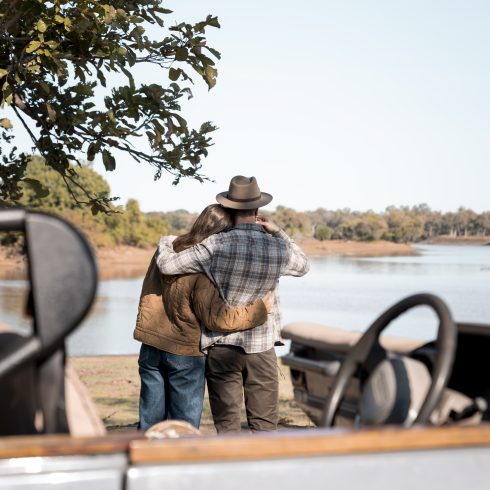Bruidspaar geniet van hun huwelijksreis met safari-uitzicht aan rivier in Zuid-Luangwa National Park, Zambia – romantisch moment bij koffiestop tijdens safari met 4x4 jeep.