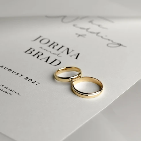 siebel-juwelier gouden trouwringen die op een save the date van een koppel ligt. De namen van het bruidspaar zijn Jorina en Brad.