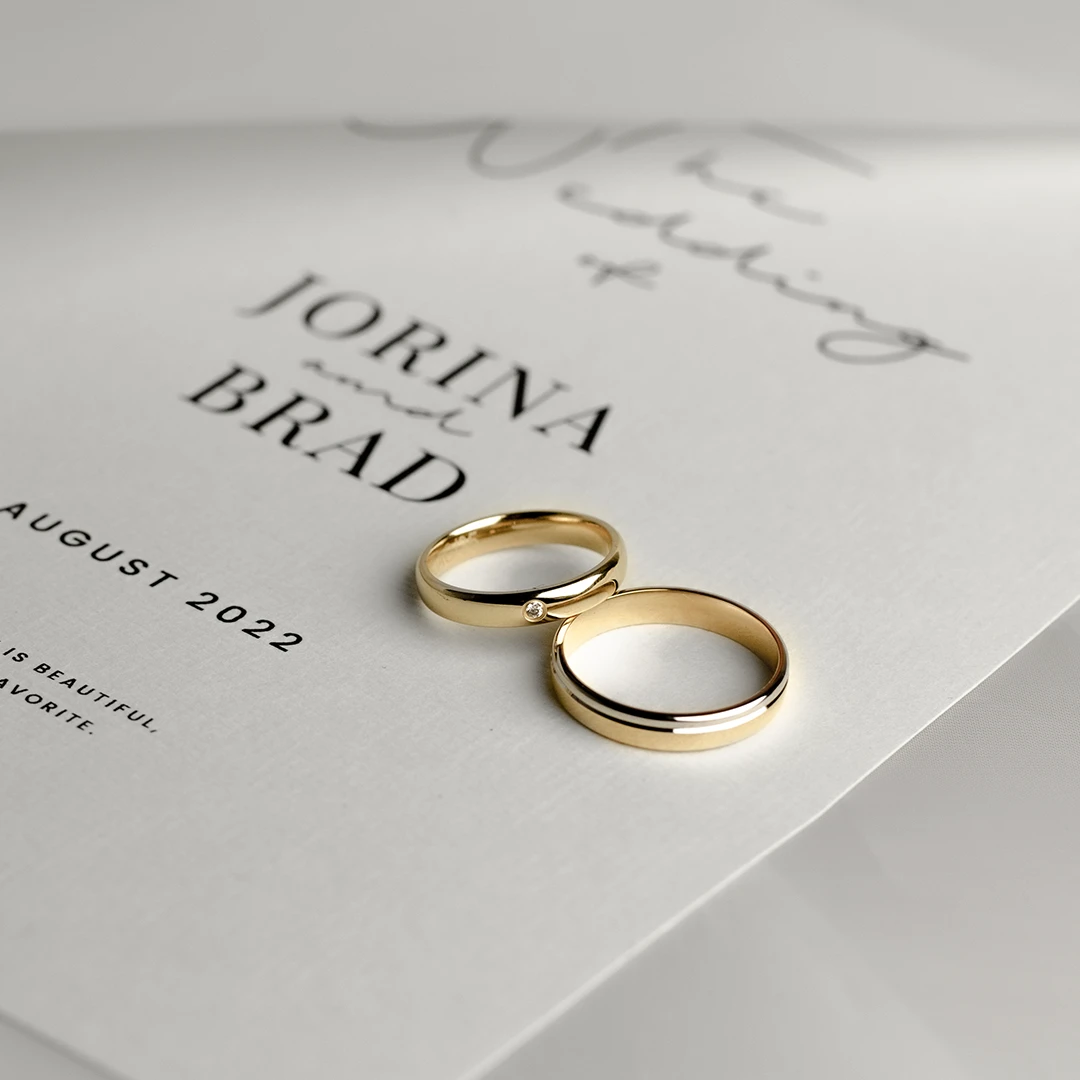 siebel-juwelier gouden trouwringen die op een save the date van een koppel ligt. De namen van het bruidspaar zijn Jorina en Brad.