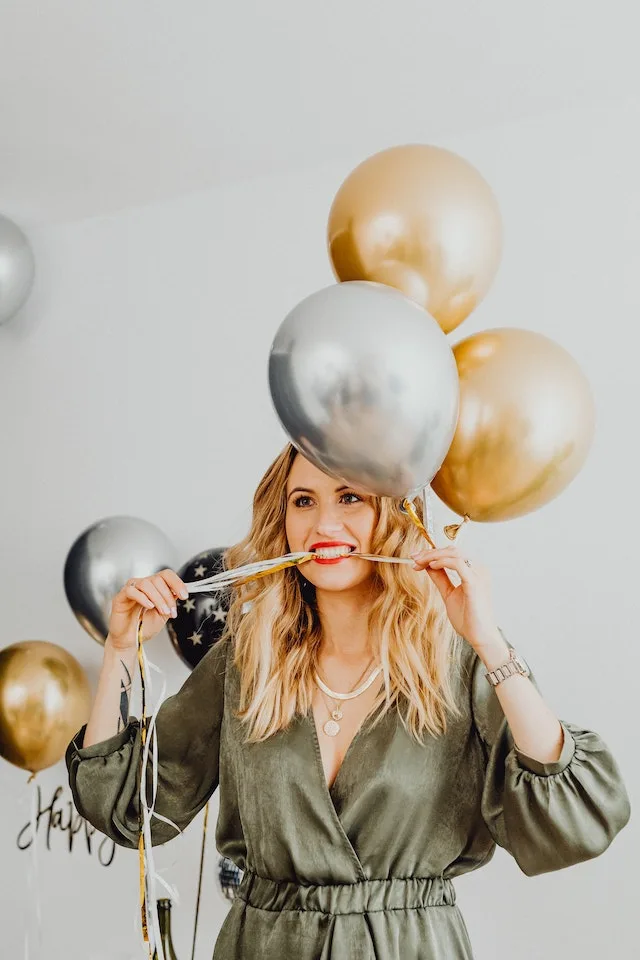 Vrouw in feestoutfit met gouden en zilveren ballonnen.