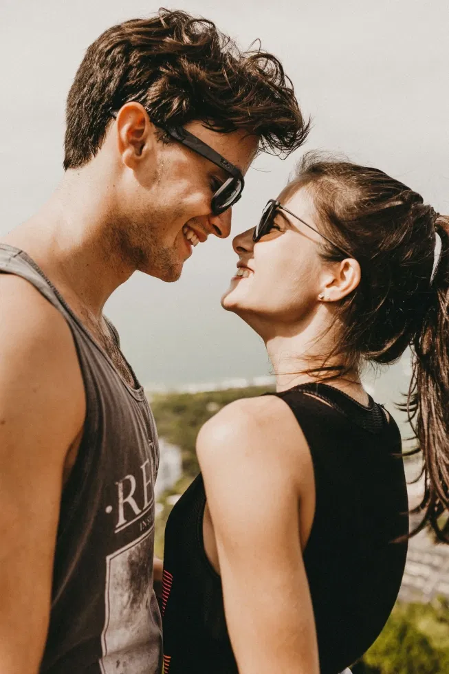 Lachend stel met tanktop en zonnebril kijken elkaar van dichtbij aan