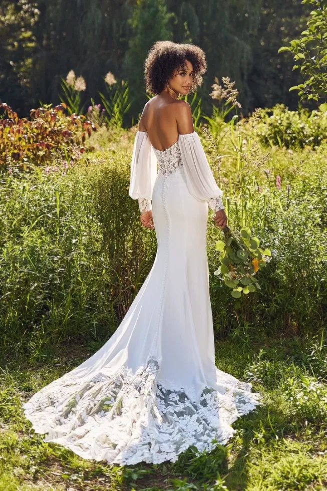 Bruid in een witte trouwjurk met kanten sleep met lange mouwen in een groen gras omgeving