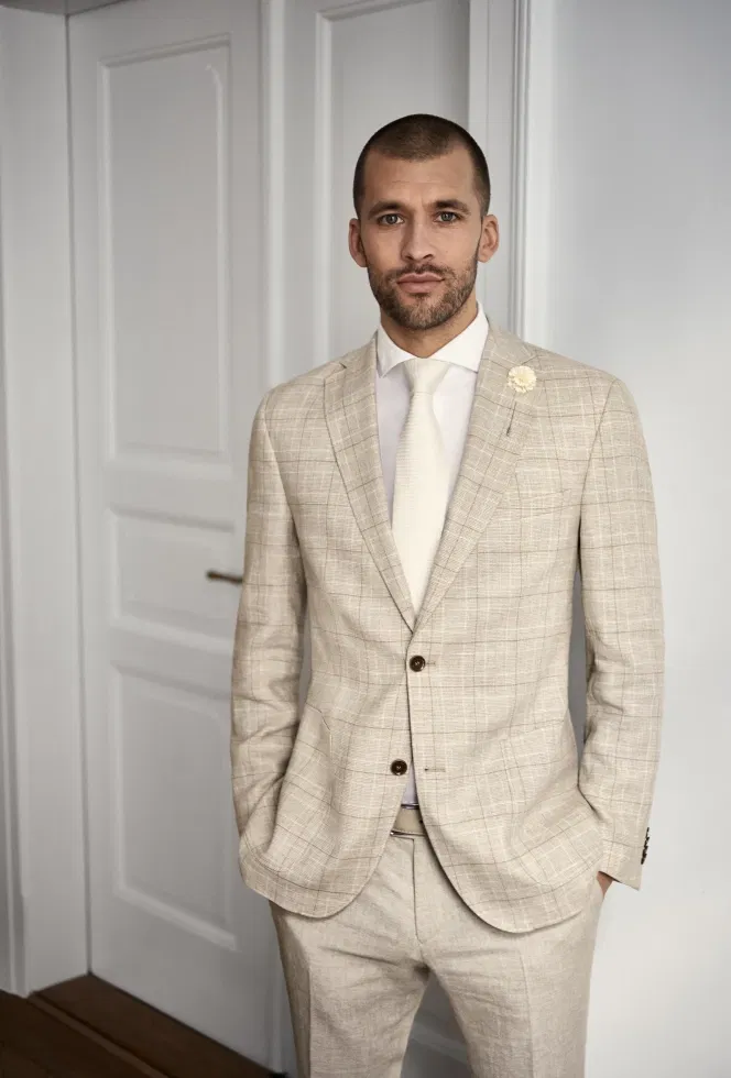 Bruidegom draagt een beige-zandkleurig tweedelig trouwpak met wit overhemd en stropdas.