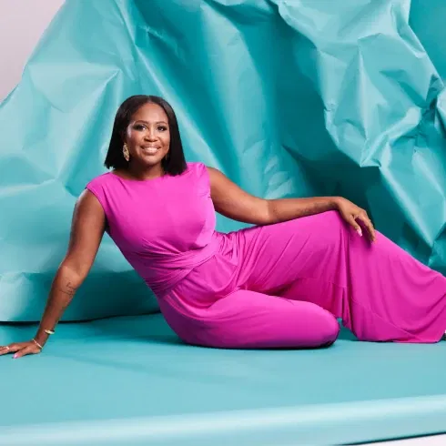 Vrouw ligt op babyblauw papier in een roze broekpak voor de dresscode cocktail