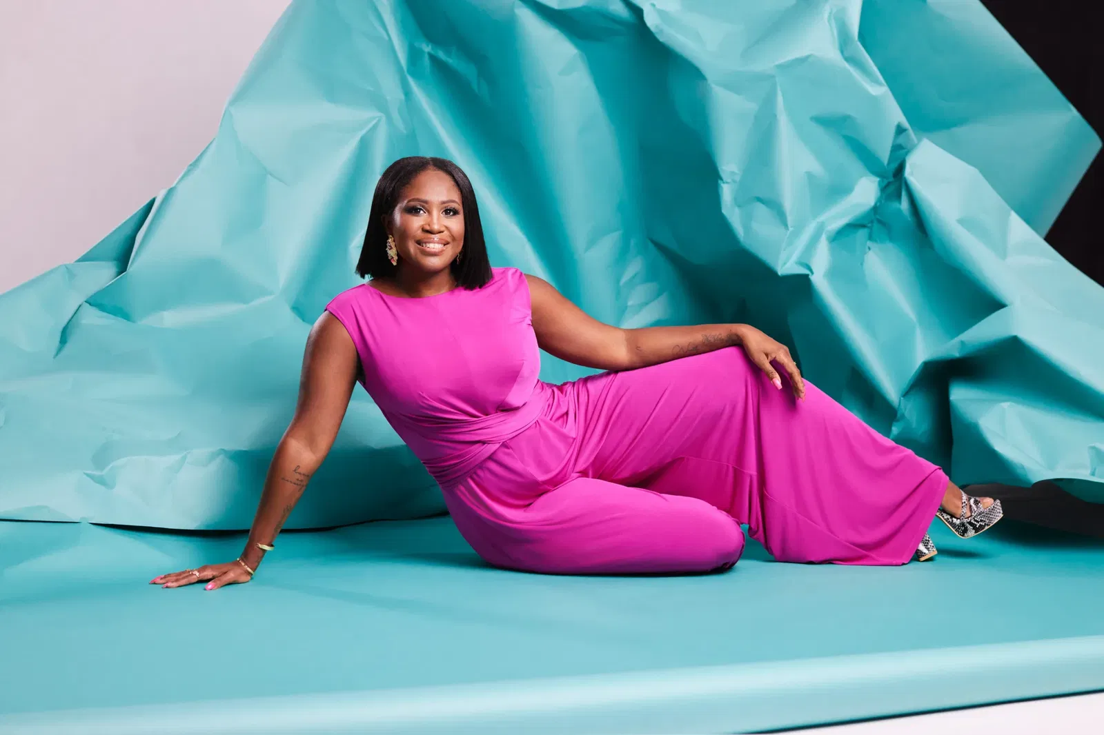 Vrouw ligt op babyblauw papier in een roze broekpak voor de dresscode cocktail