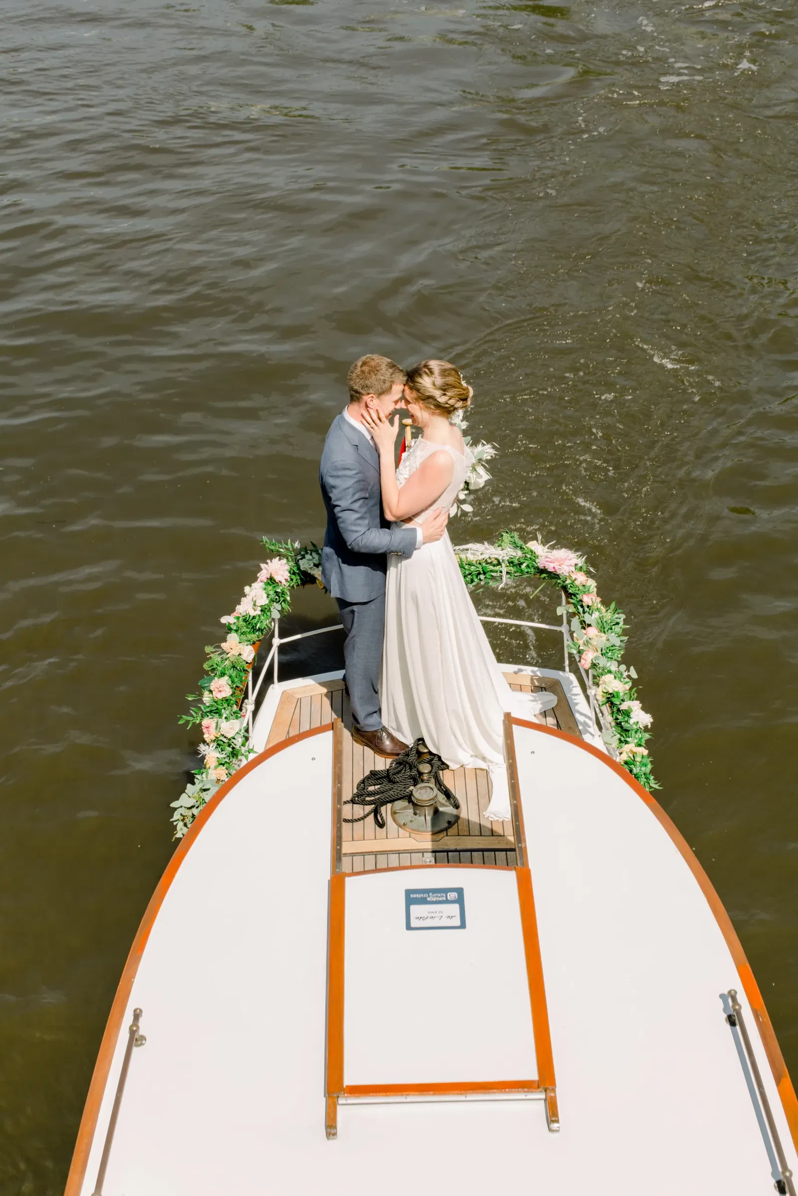 Het bruidspaar staan met hun hoofden tegen elkaar achterop het dek van de Salonboot De Liefde