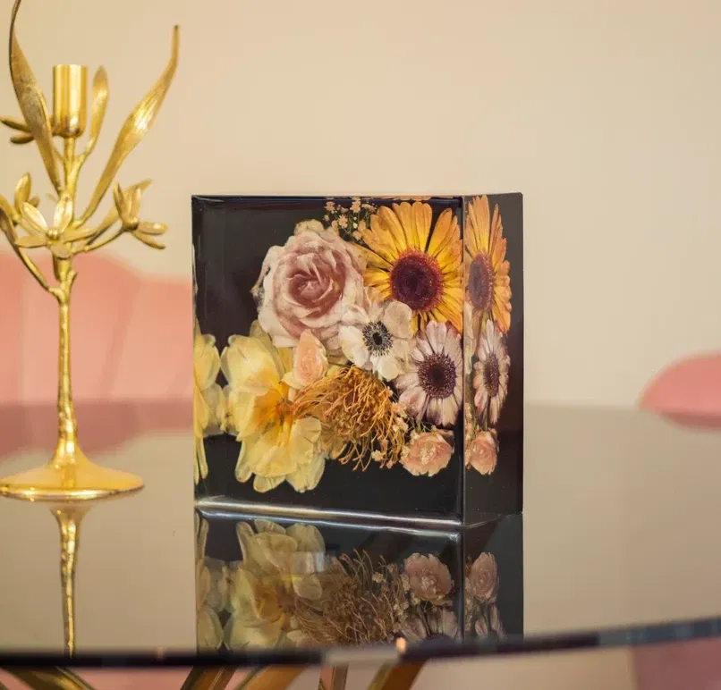 Bruidsboeket in vierkant epoxy blok op glazen eettafel met een gouden kandelaar er naast.