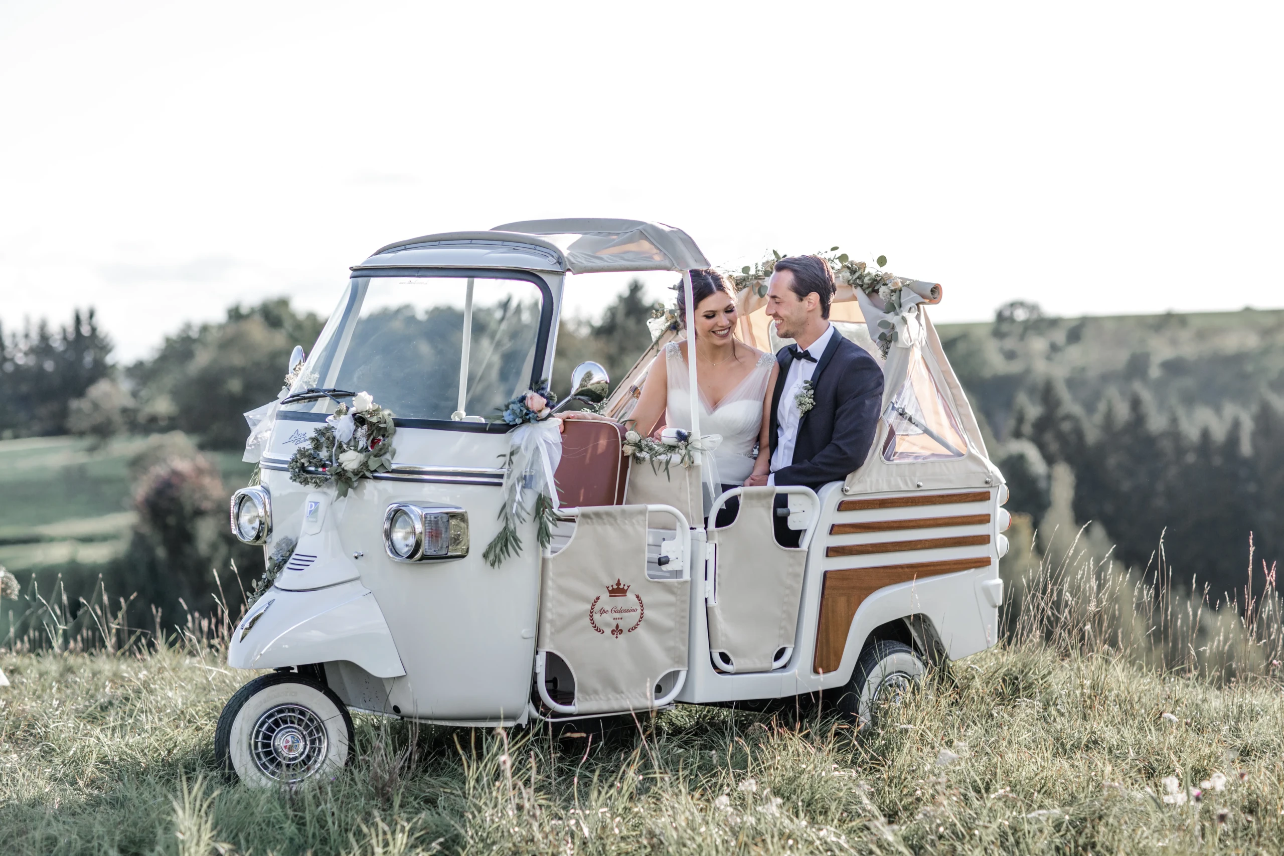 Bruidspaar zit in een witte met bloemen versierde tuktuk cabrio.
