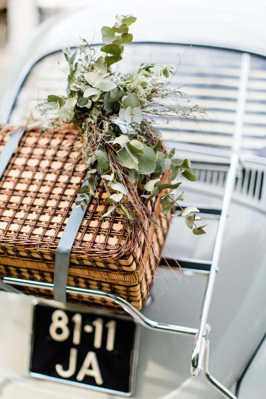 Rieten gevlochten mand met bloemen achterop een rek van een klassieke witte trouwauto