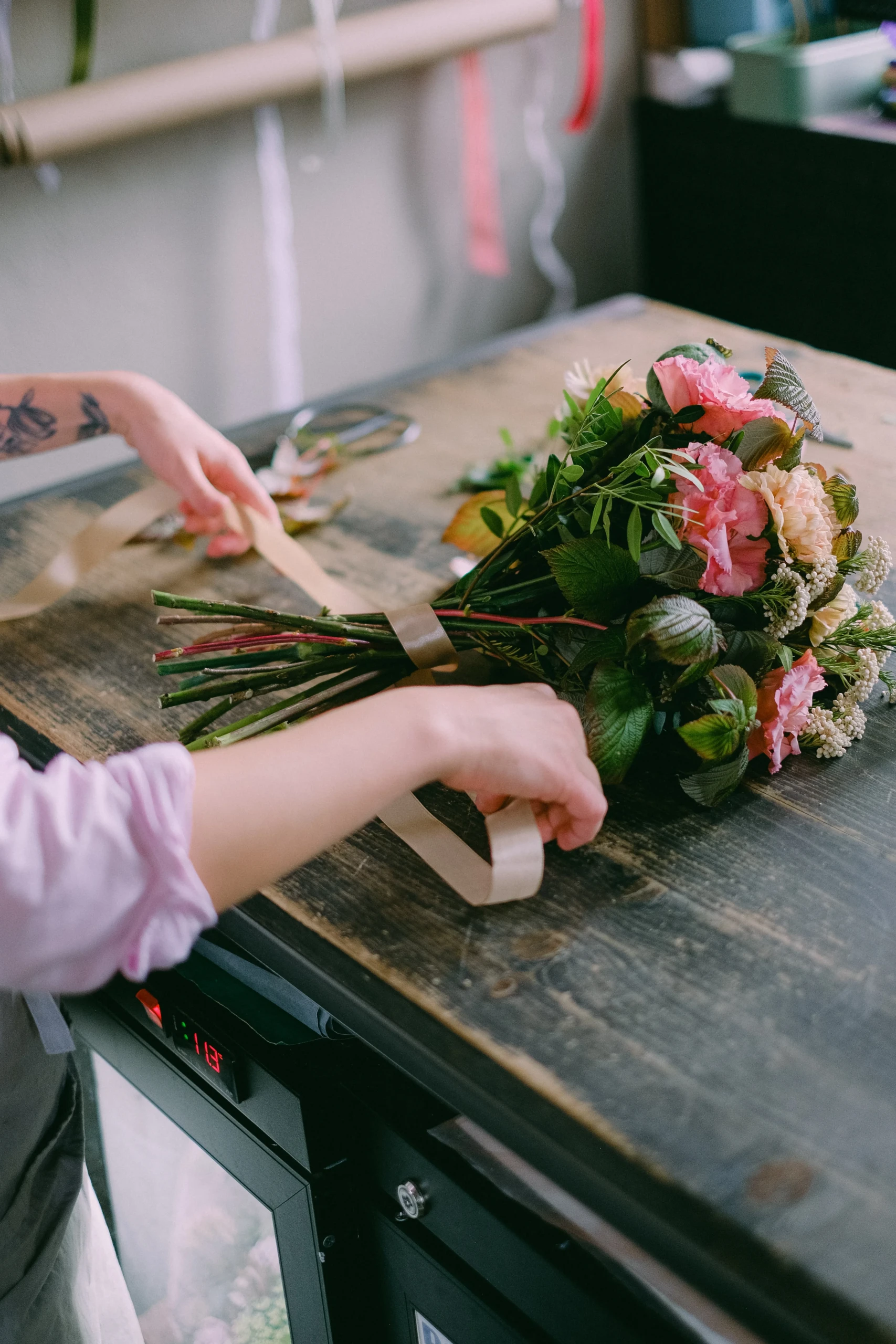 Twee handen voorzien een fleurig boeket van een lichtroos lint
