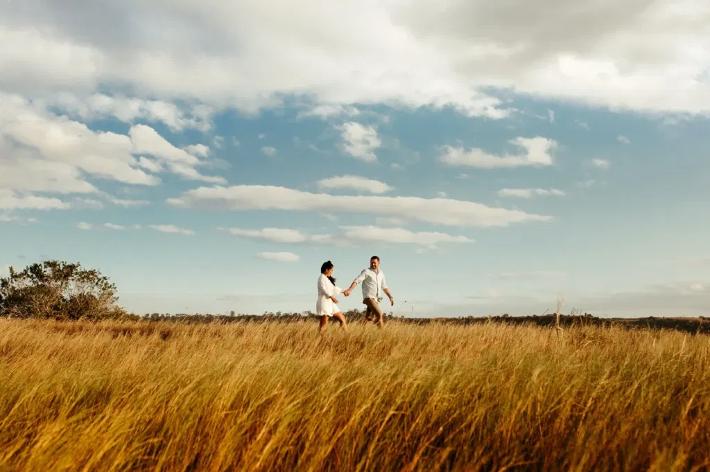 man en vrouw lopen gearmd door hoog grasland gearmd. Boven hun blauwe lucht met witte wolken
