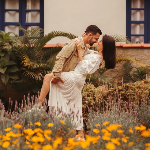 In een tuin houdt de man een been van vrouw omhoog leunend naar voren terwijl de vrouw de man in zijn nek omarmd