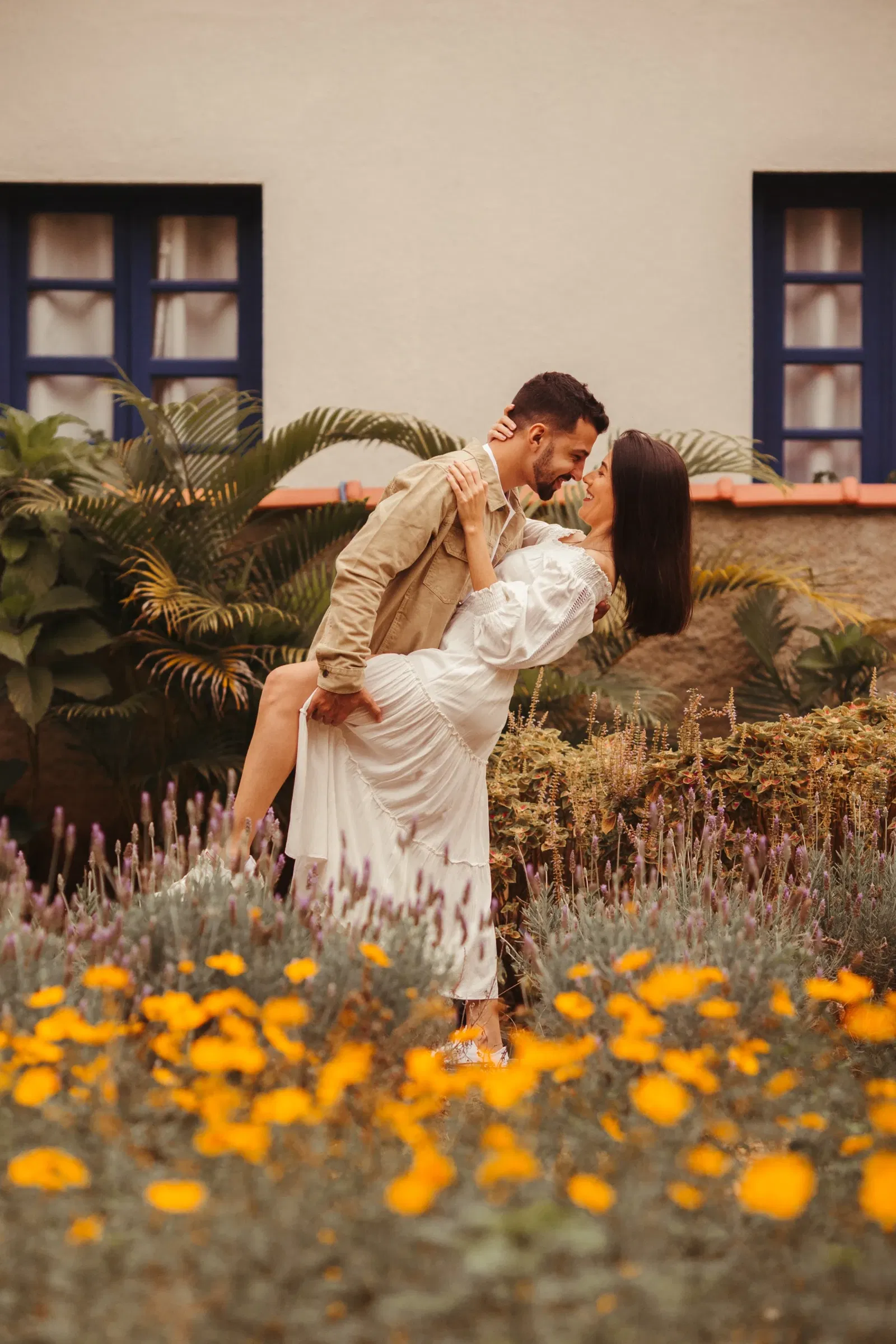 In een tuin houdt de man een been van vrouw omhoog leunend naar voren terwijl de vrouw de man in zijn nek omarmd