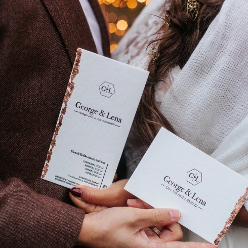 In de handen van het bruidspaar een trouwkaart en een save the date kaart.
