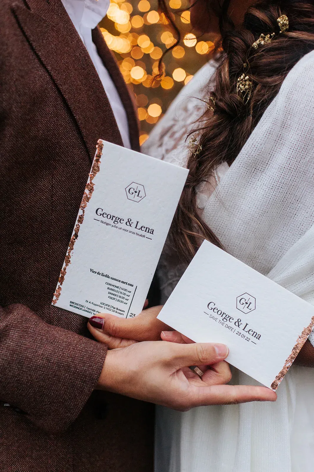 In de handen van het bruidspaar een trouwkaart en een save the date kaart.