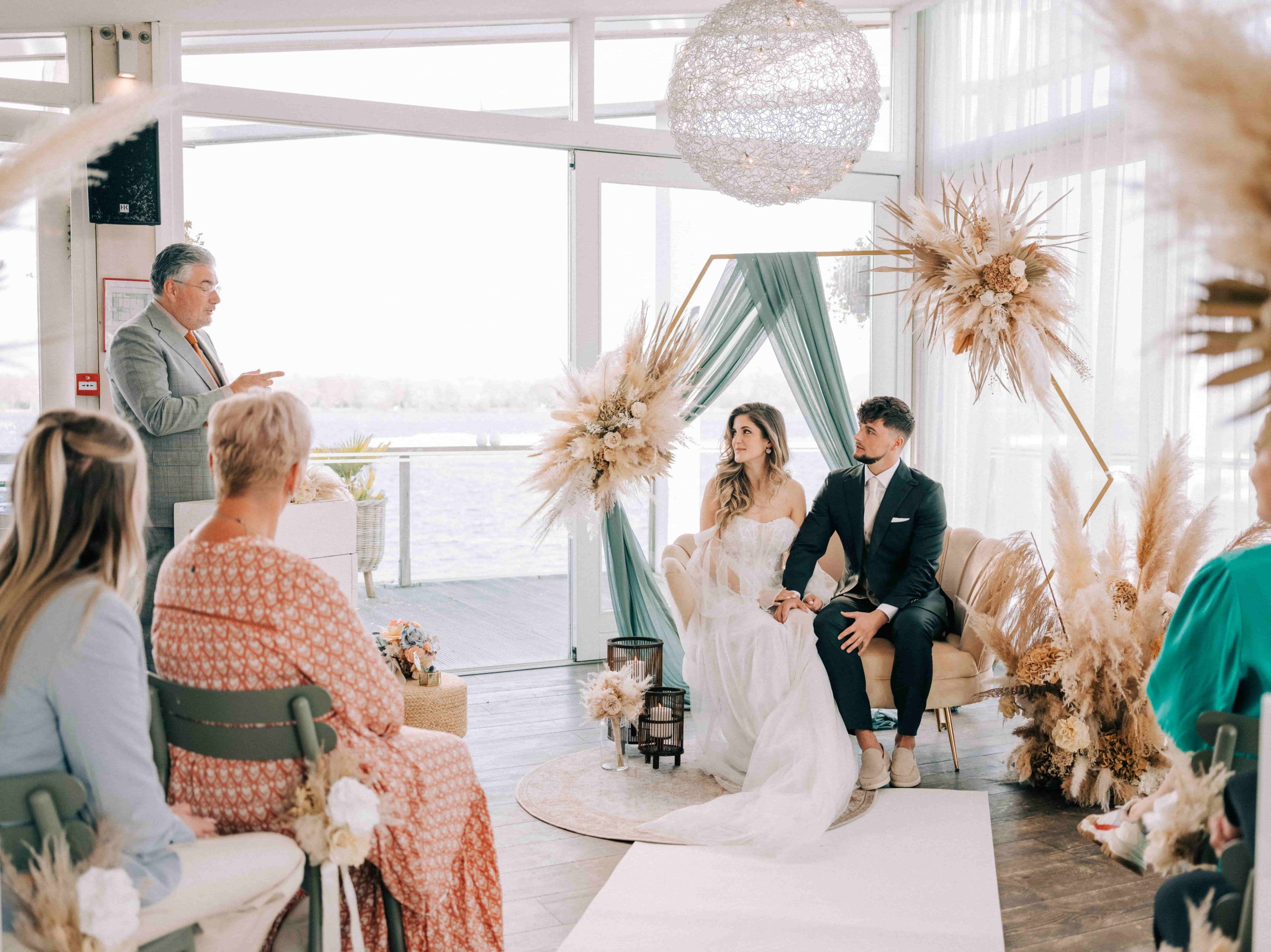 Bruidspaar wordt tijdens de huwelijksceremonie toegesproken. Bruid en bruidegom zitten naast elkaar op de bank