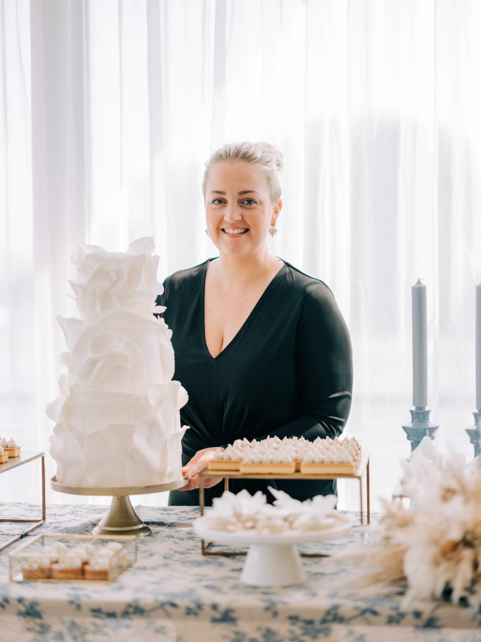 lachende vrouw in zwarte jurk achter een geheel witte bruidstaart