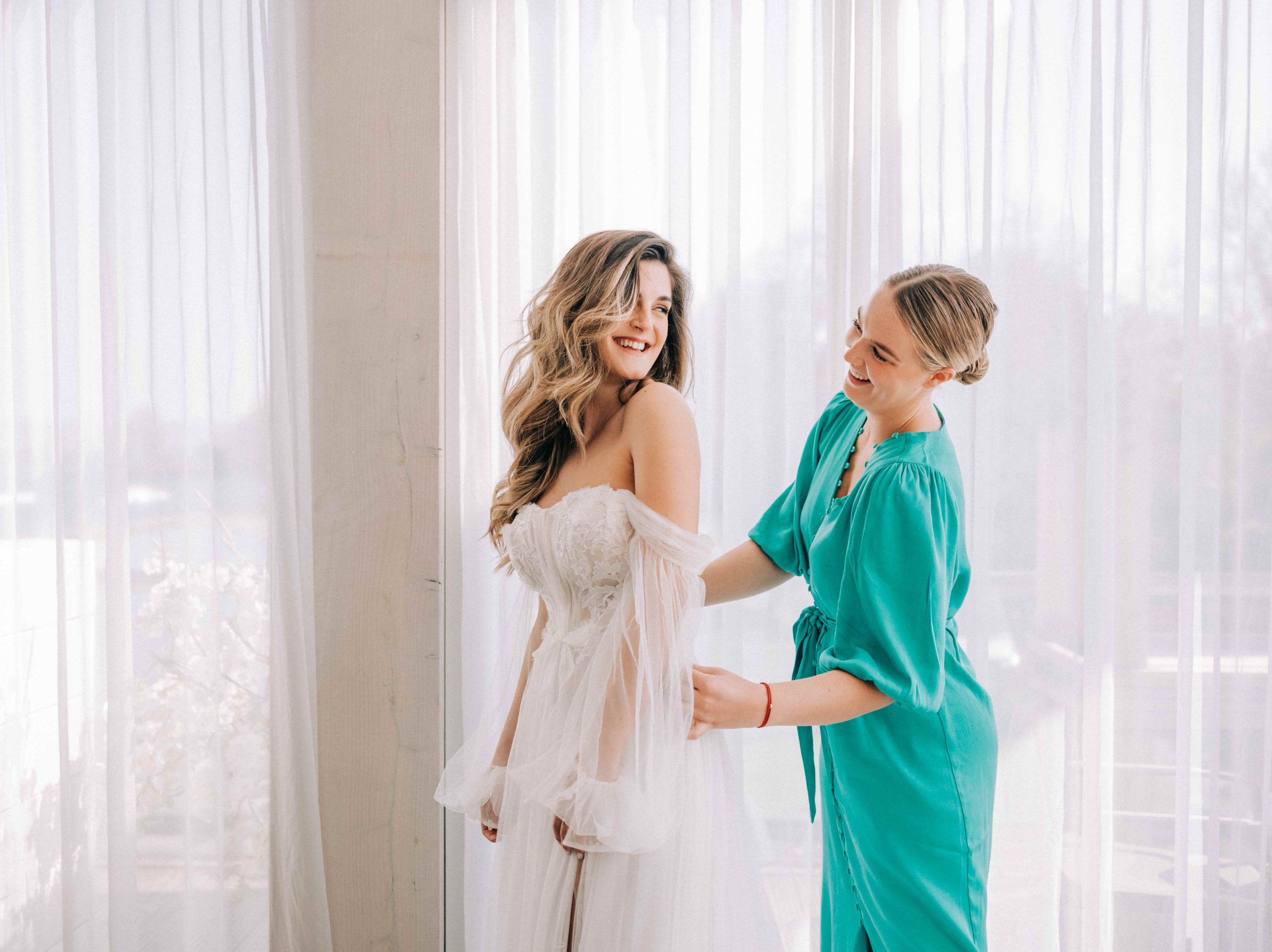 vrouw in mintgroene jurk maakt de sluiting van de trouwjruk vast.