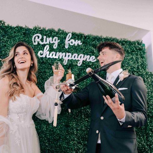 Bruidegom ontkurkt de champagne fles met een sabel. Bruid houdt champagneglas lachend vast