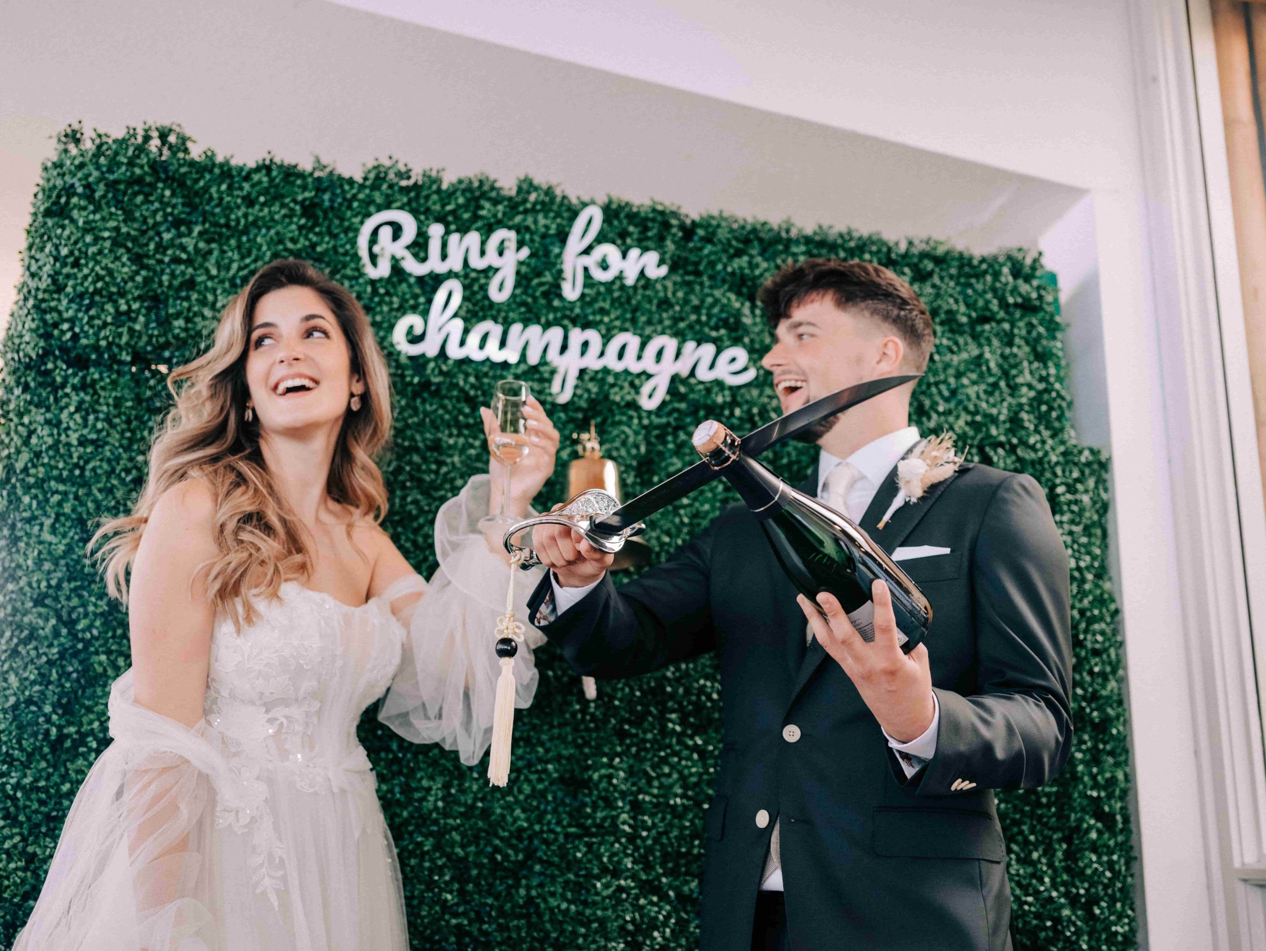 Bruidegom ontkurkt de champagne fles met een sabel. Bruid houdt champagneglas lachend vast