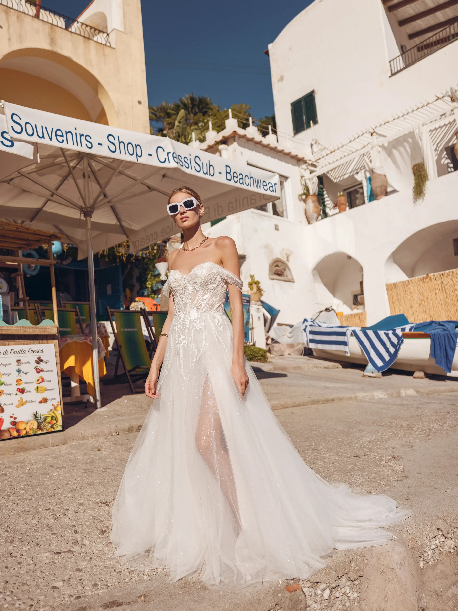 Bruid met een witte vierkante zonnebril loopt over het Griekse strand in een bruidsjurk van Modeca uit de collectie Blissful Collection_Banu