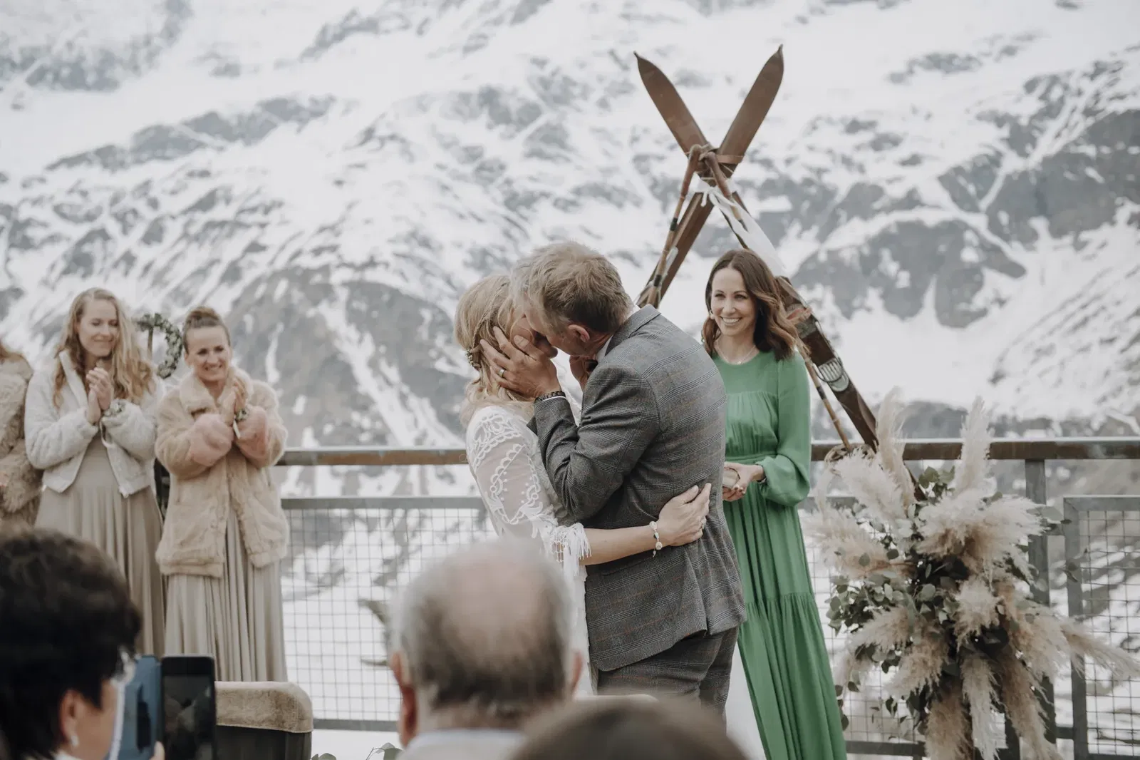 Bruid en bruidegom kussen elkaar tijdens een ceremonie in de sneeuw met bergen op de achtergrond.