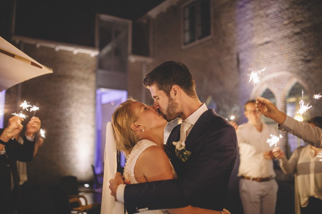 Bruid en bruidegom delen een romantische kus omringd door gasten met sterretjes tijdens een avondbruiloft.