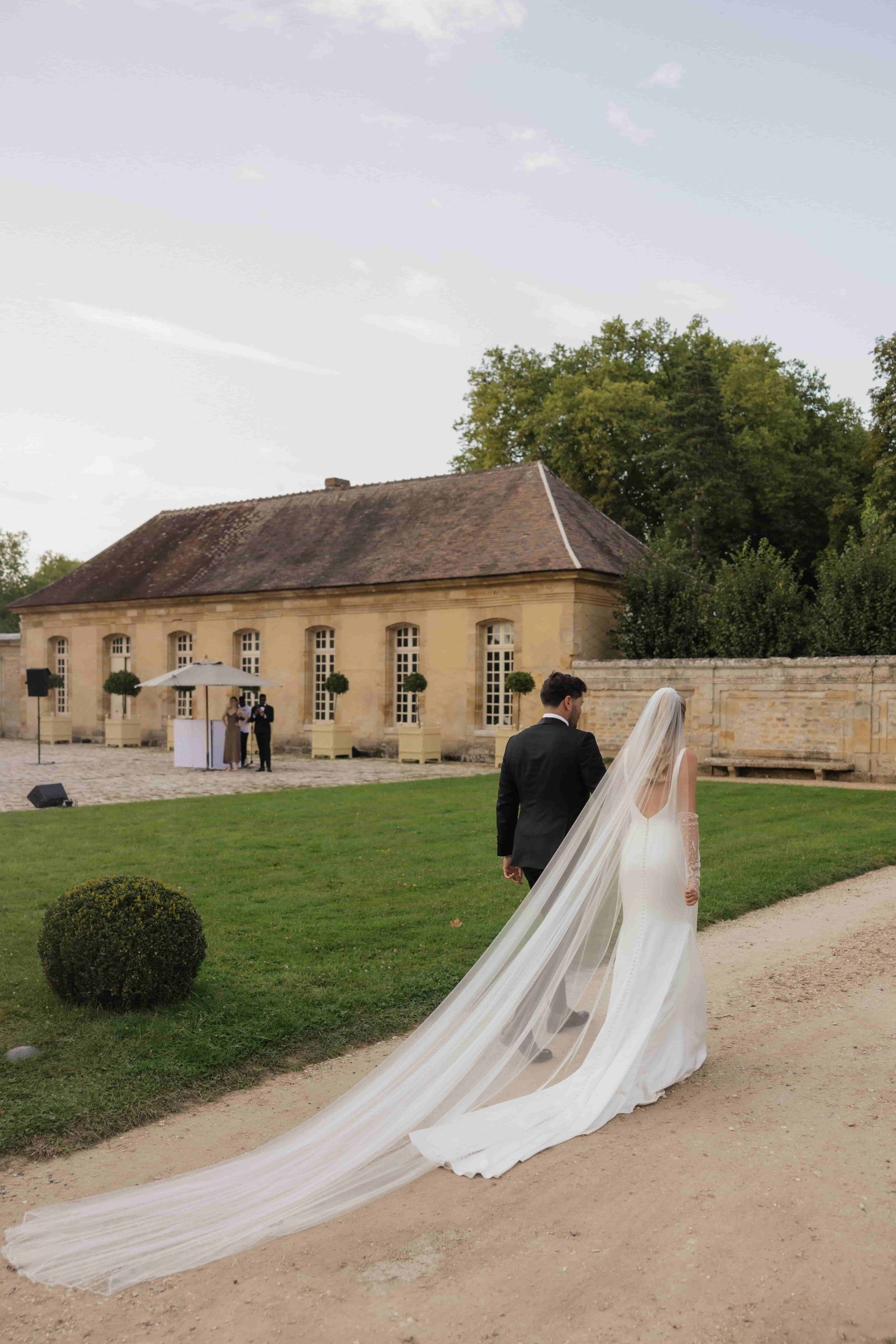 Bruidspaar Hannah Godwin en Dylan Barbour voor hun trouwlocatie. Bruidsjurk met prachtige lange sleep en sluier.