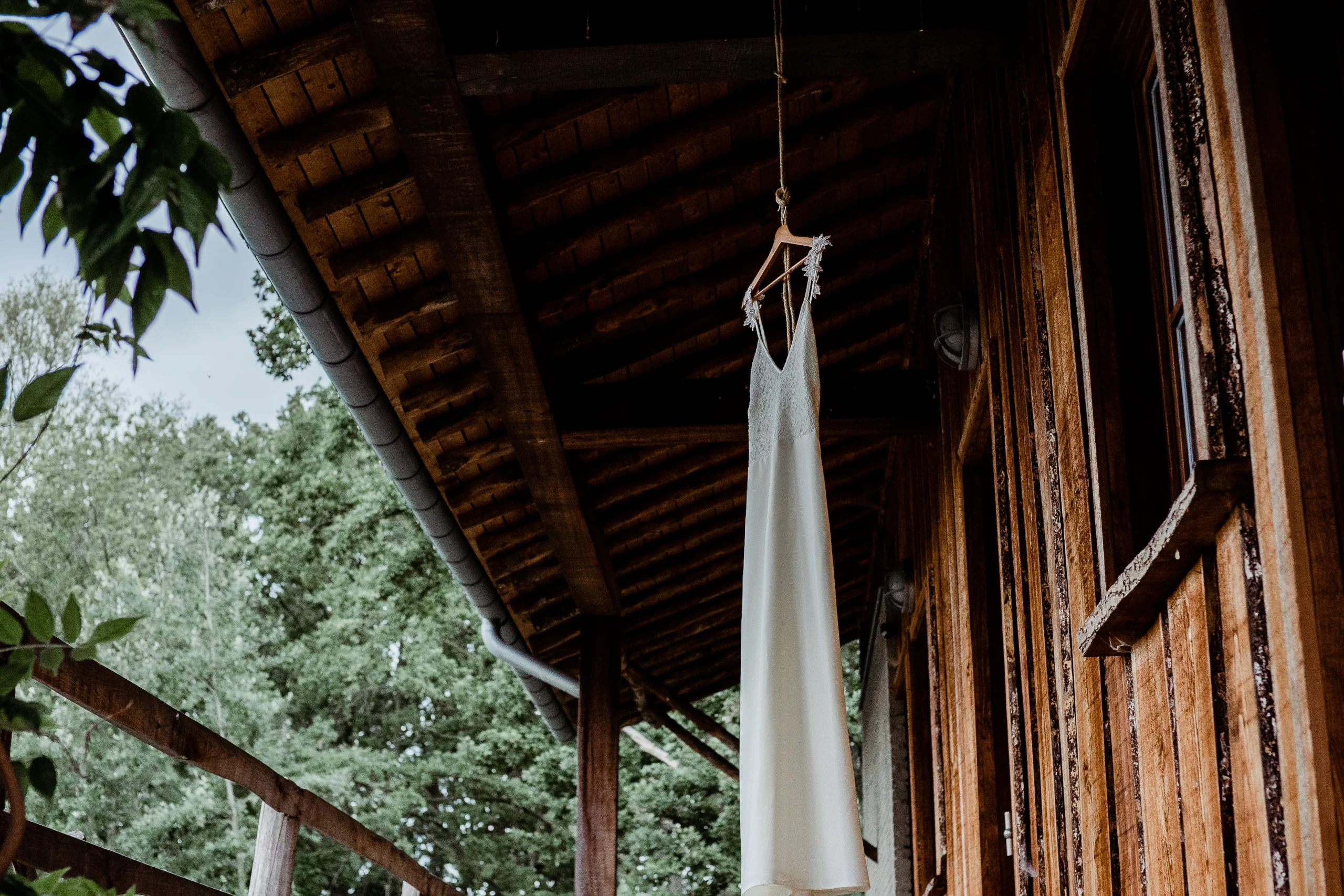 Bruidsjurk hangt aan haak, buiten, Houten hut als trouwlocatie.