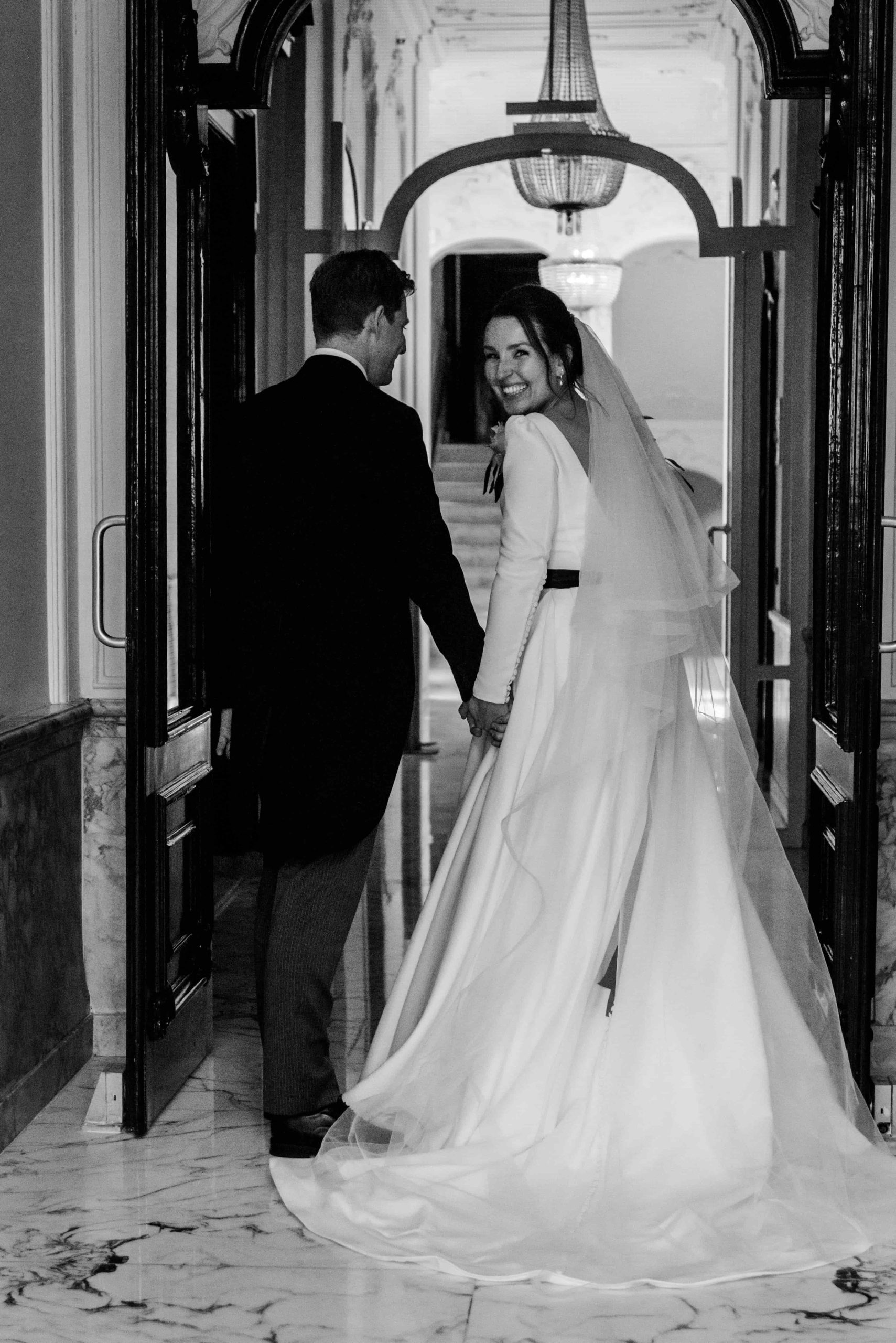 Zwartwit foto van bruidspaar, bruid kijkt vrolijk achterom.