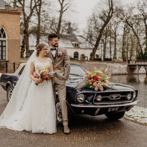 Bruidspaar voor hun trouwauto, een zwarte oldtimer.