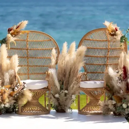 twee grote rieten rotan stoelen voor bruidspaar aan het strand voor een strandbruiloft.