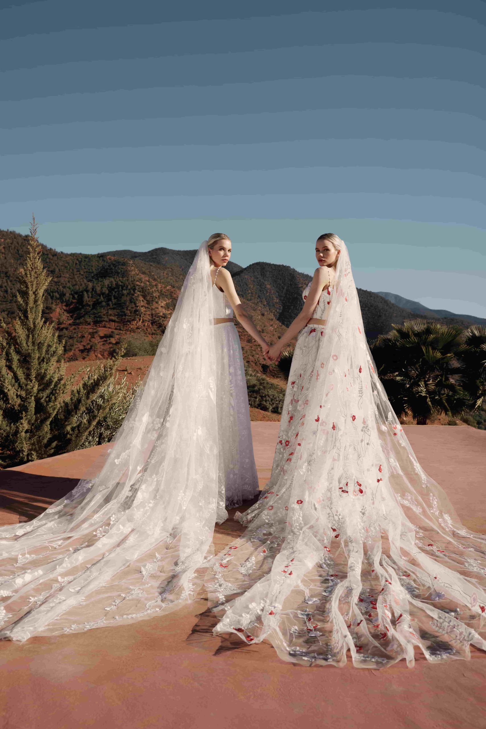 Twee bruiden hand in hand in de woestijn met prachtige bruidskleding en lange sluiers van Poirier.