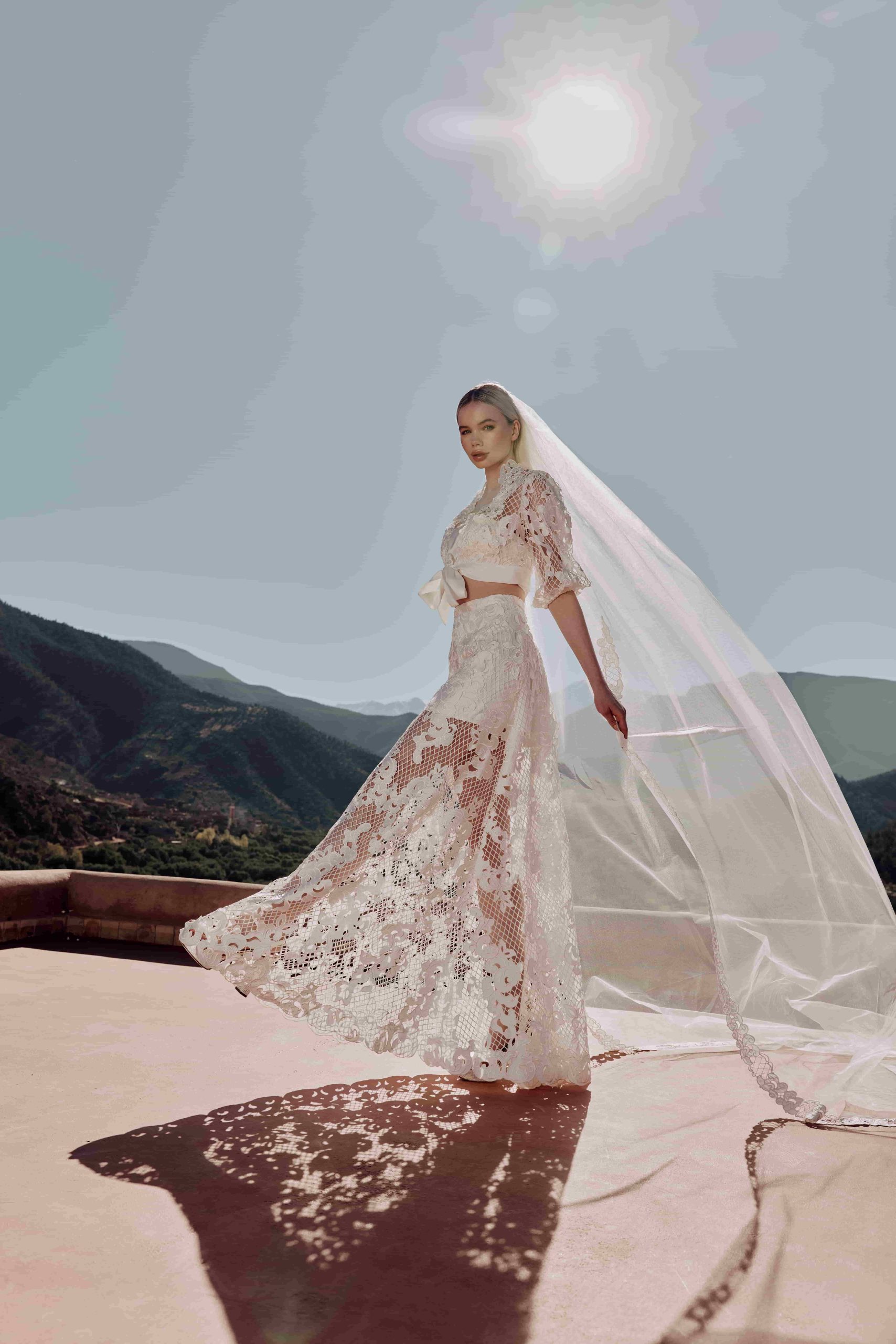 Bruid in de woestijn met blauwe lucht en een schijnende zon. Ze draagt een boho bruidsoutfit met een prachtige lange sluier van Poirier.