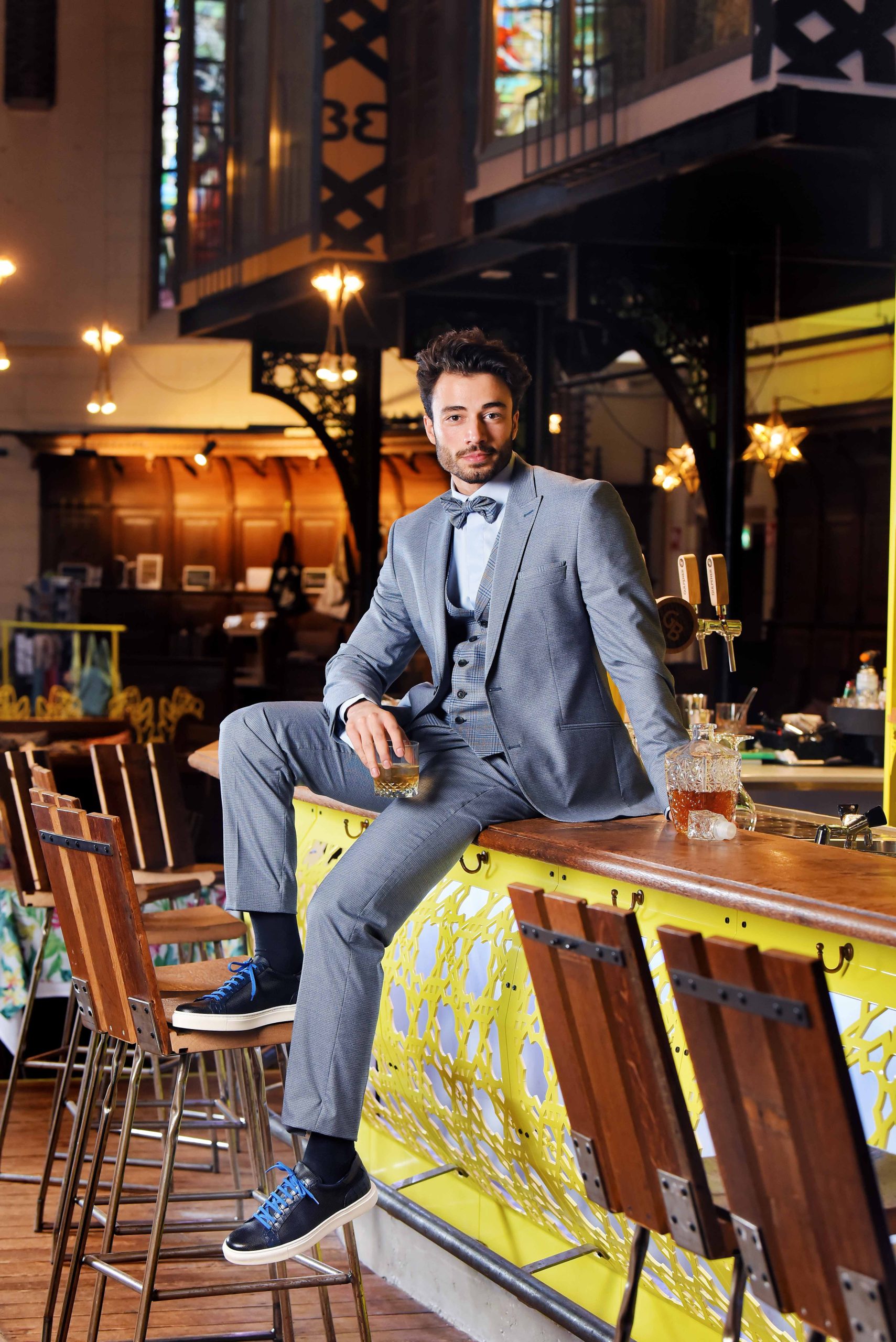 Bruidegom in blauw pak, zitten op de bar met een whisky in de hand.