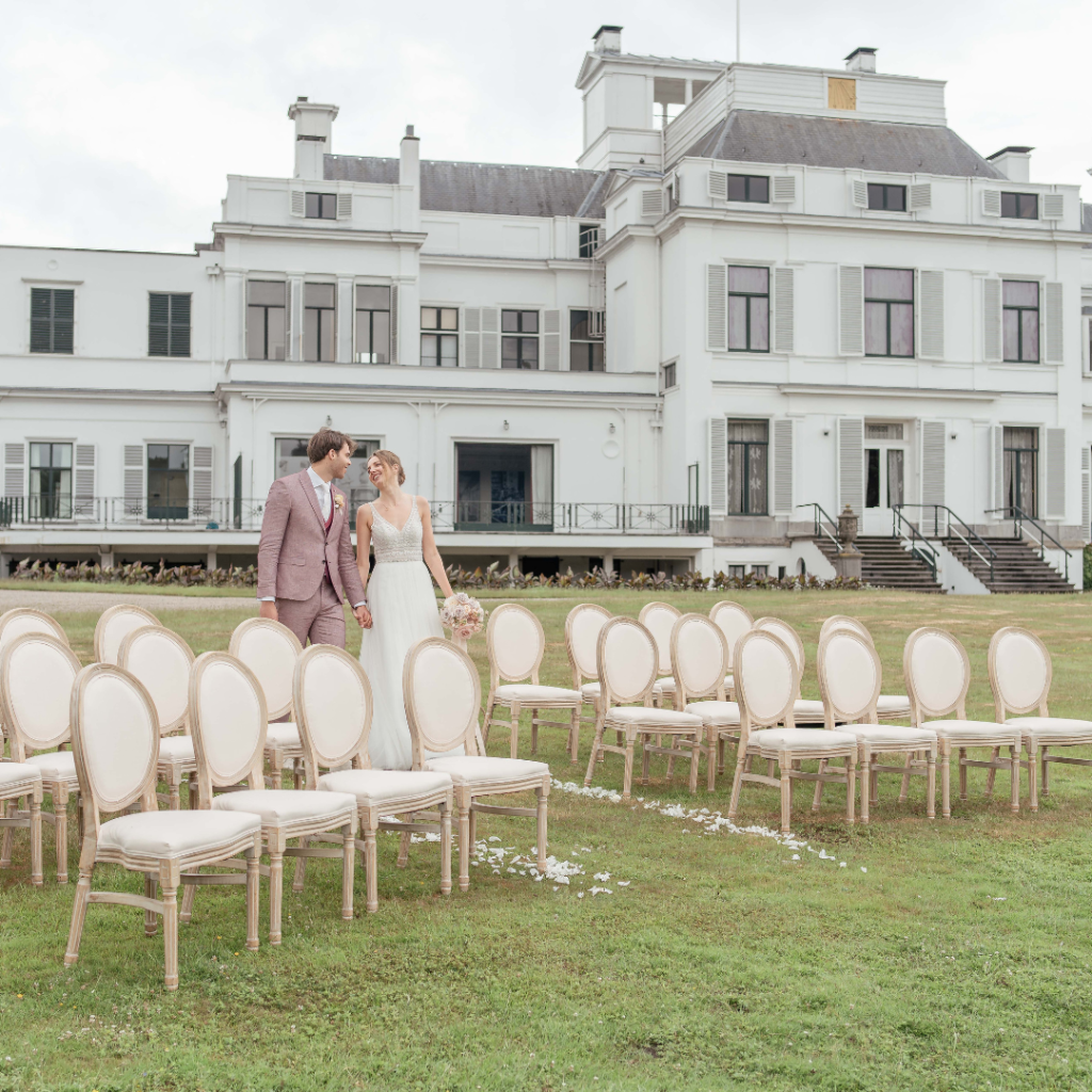 Trouwlocatie. Groot landhuis met stoelen in ceremonie-opstelling op de voorgrond.
