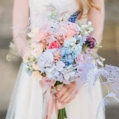 Een bruid in een witte jurk een groot bruidsboeket vol pastelkleurige bloemen