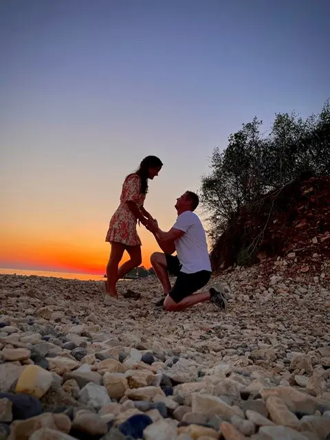 Jong stel op het strand met zonsondergang. Man op één knie, doet een aanzoek.