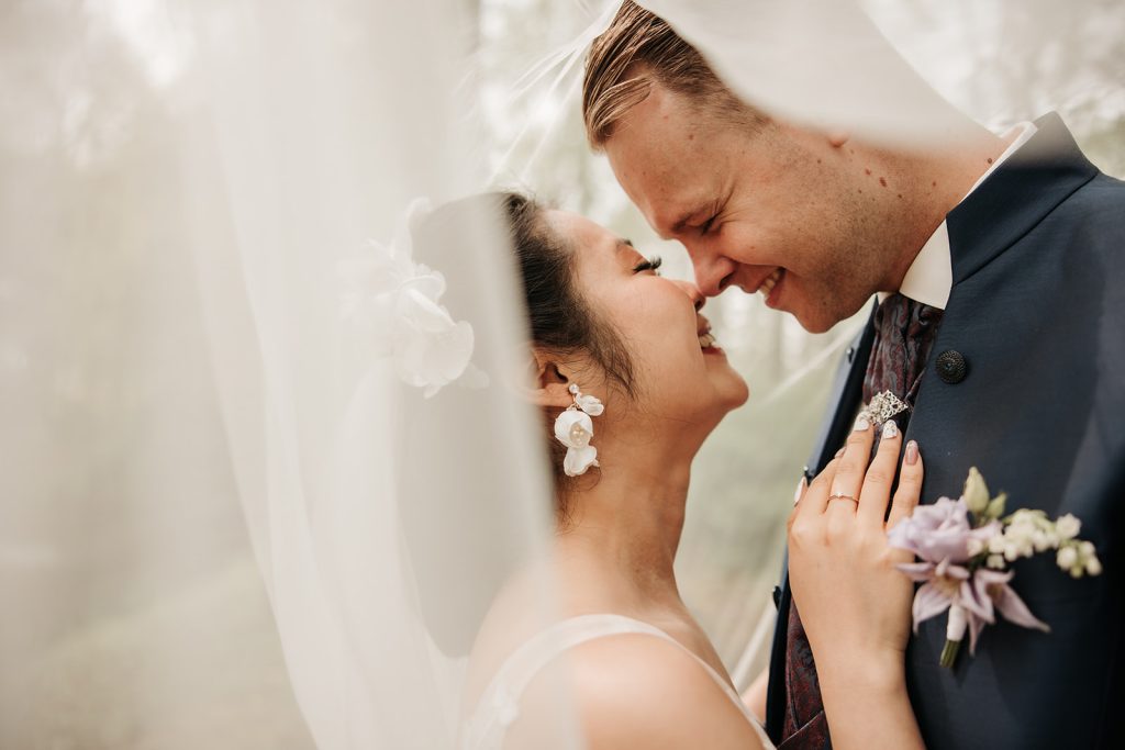 Bruidspaar onder sluier kijkt elkaar verliefd aan,