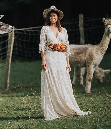 boho-bruid omringd door lama's in kanten jurk en bloemenriem