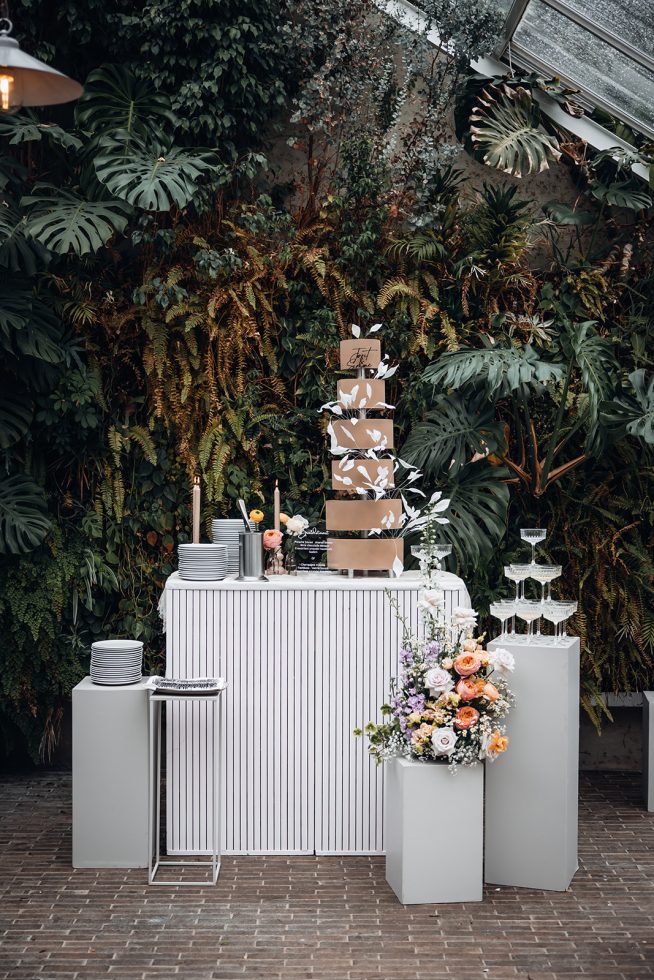 Zeslaagse bruidstaart met bloemen en champagnetoren.