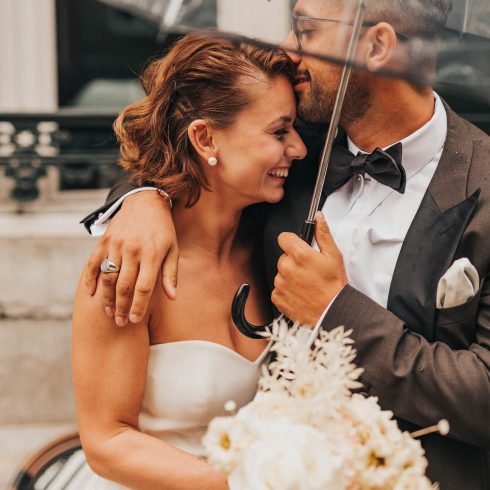 Bruidspaar onder paraplu. Bruidegom kust zijn bruid op haar voorhoofd.