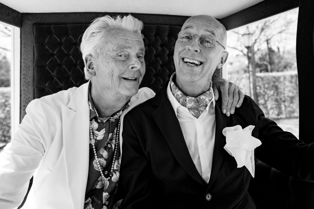 Bruidegoms in koets, kijken vrolijk naar de camera