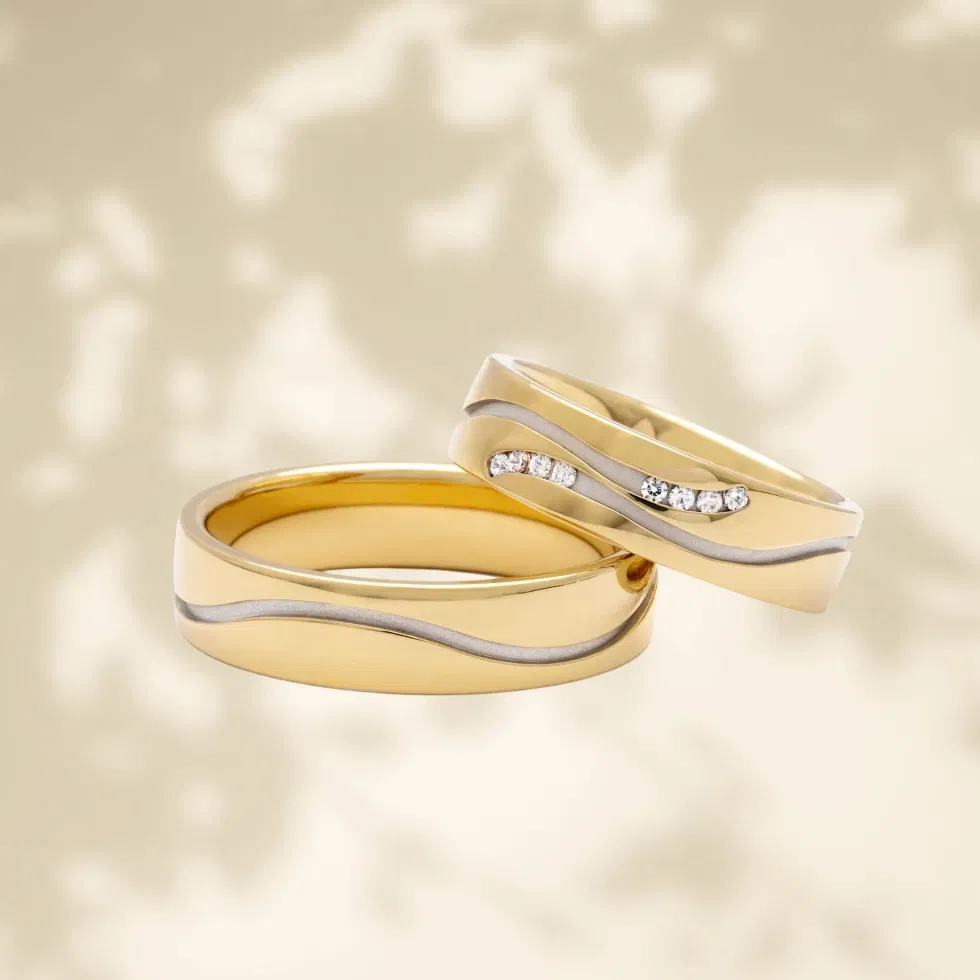 Set van twee gouden trouwringen met een elegante golvende zilverkleurige lijn. Eén van de ringen is bezet met meerdere glinsterende diamanten.