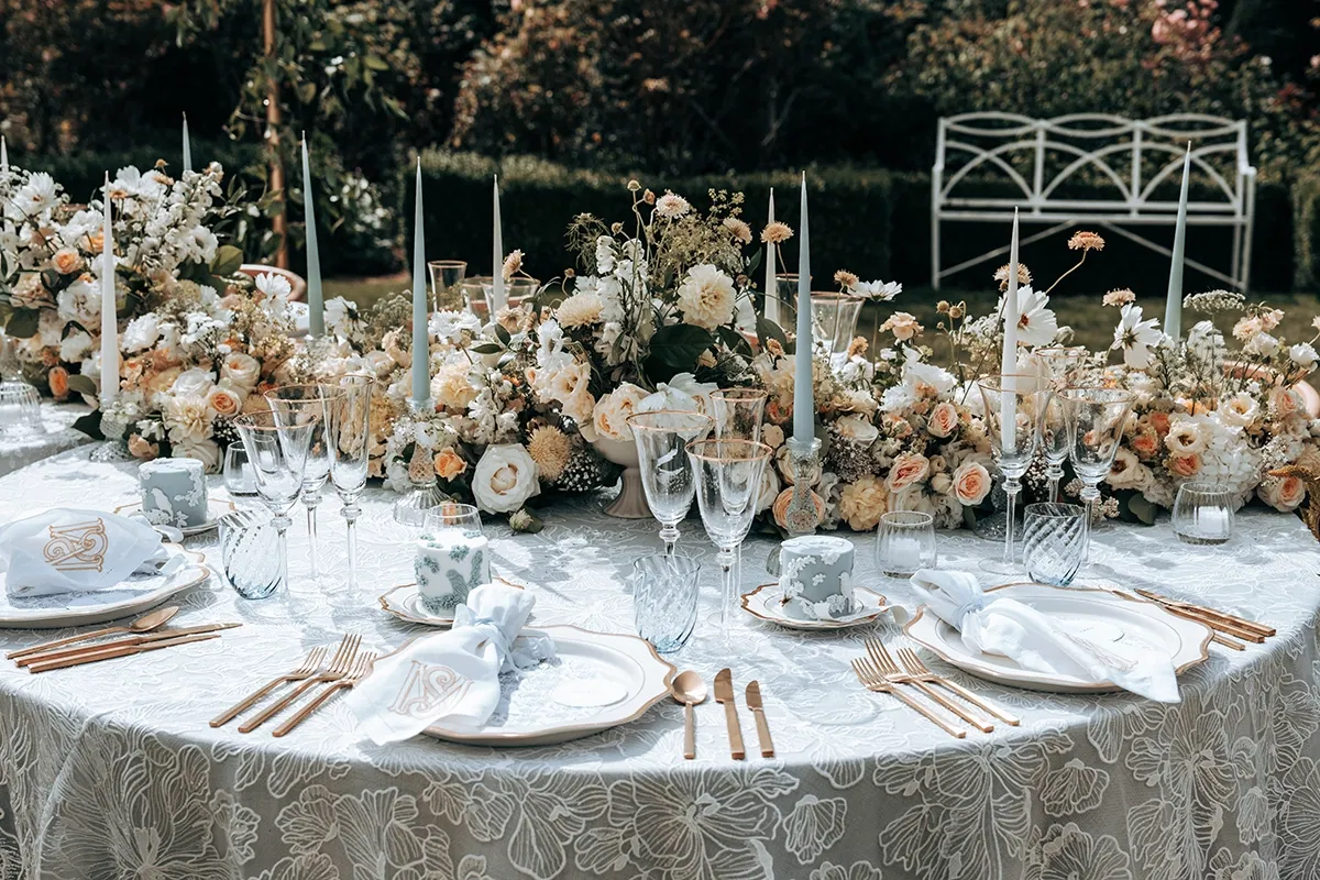 gedekte tafel voor bruidsdiner met gepersonaliseerde servetten, luxe servies en een zee aan bloemen en kaarsen.