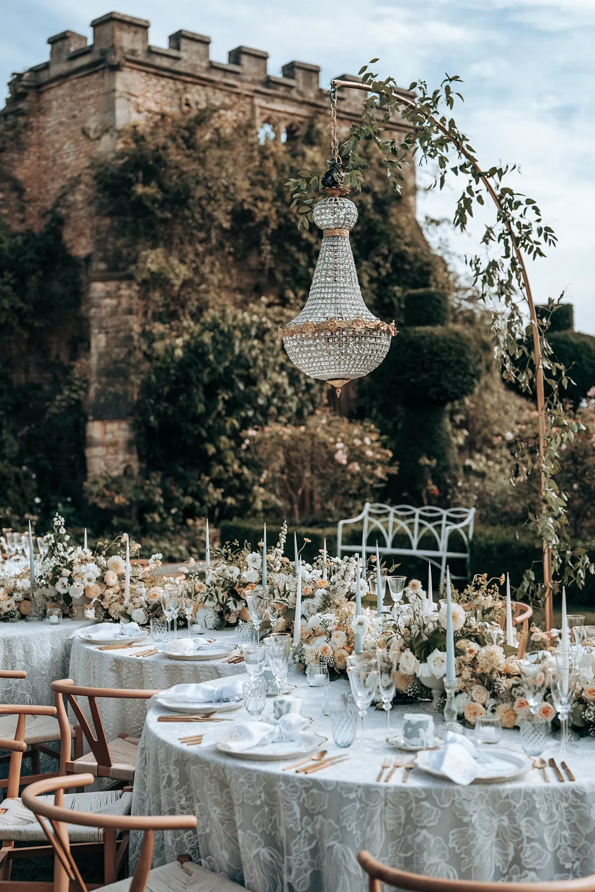 gedekte tafel voor bruidsdiner met gepersonaliseerde servetten, luxe servies en een zee aan bloemen en kaarsen. Landhuis en kroonluchters buiten.