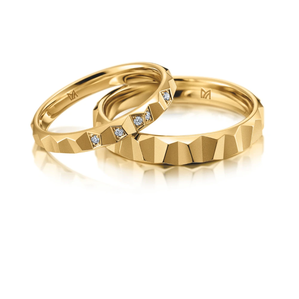 Drie geelgouden trouwringen met een opvallend facetontwerp. Eén ring is versierd met sprankelende diamanten voor een moderne en luxueuze uitstraling.