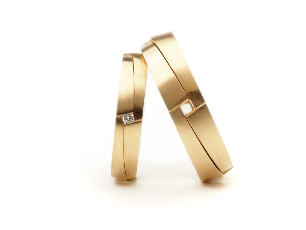 Twee gouden trouwringen met een moderne afwerking, één ring met een diamant en de andere met een geometrisch vakje.