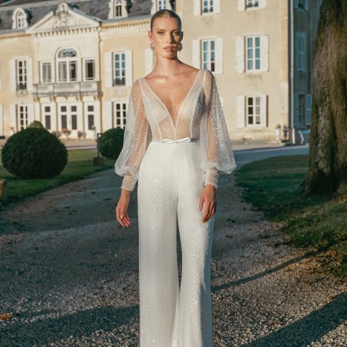 Bruid met een wit jumsuit aan met een doorschijnend bovenlijfje en mouwen.