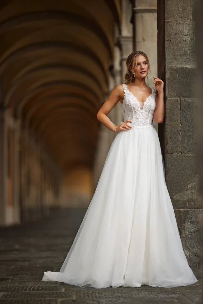 Bruid in een verfijnde A-lijn trouwjurk met kanten top en diepe V-hals, poserend onder een historische booggalerij.